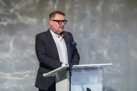 Na zdjęciu Jarosław Klimaszewski, prezydent Bielska-Białej, otwiera konferencję **"Kultura dla Zdrowia i Dobrostanu"**. Stoi przy mównicy, ubrany w elegancki garnitur, przemawiając do zgromadzonych. W tle widać subtelnie oświetloną scenę z abstrakcyjną projekcją.